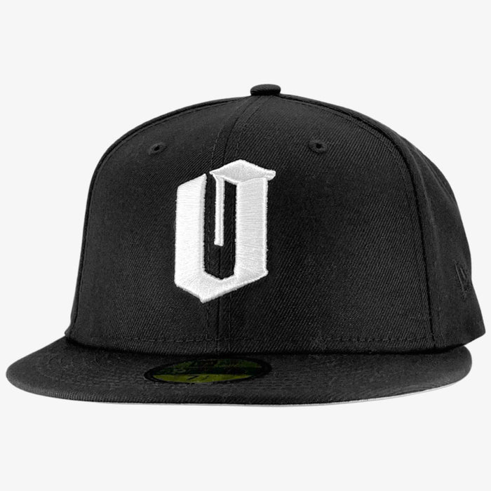 A black New Era Official 59FIFTY Fitted Cap featuring a prominent white embroidered “U” on the front. The structured crown and signature round sticker emphasize its authenticity, while a plain light gray background brings focus to the Oaklandish-inspired design. Brand: Other.