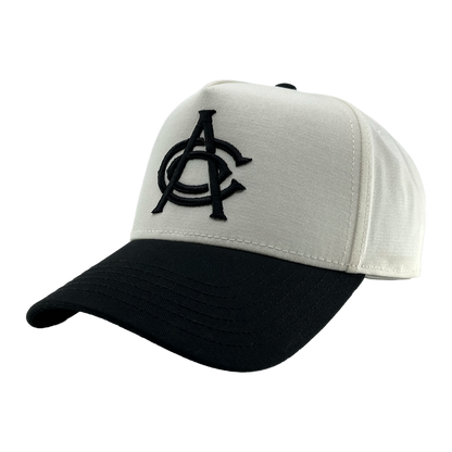A white and black OAC Logo 5 Panel snapback cap with a curved black brim. The structured front showcases large, overlapping black embroidered “OAC” letters in a bold font—clearly representing the OAC brand. The cap is displayed against a plain, light gray background.