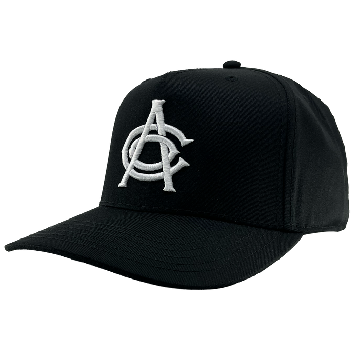 The OAC Logo 5 Panel by OAC is a black snapback cap with a curved brim, featuring large, white, intertwined embroidered letters “A” and “C” on the front panel to represent the Oakland Athletic Club. The plain white background emphasizes the cap’s structure and its distinctive embroidered logo.
