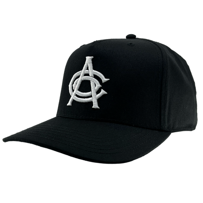 The OAC Logo 5 Panel by OAC is a black snapback cap with a curved brim, featuring large, white, intertwined embroidered letters “A” and “C” on the front panel to represent the Oakland Athletic Club. The plain white background emphasizes the cap’s structure and its distinctive embroidered logo.