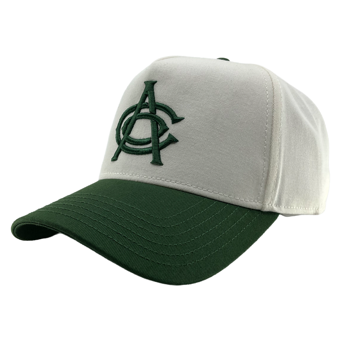 The OAC Logo 5 Panel by OAC is a white snapback cap with a dark green brim, featuring an embroidered green interlocked “A” and “C” logo on the front for the Oakland Athletic Club. Visible stitching accents the bill and crown, and it’s shown against a plain white background.
