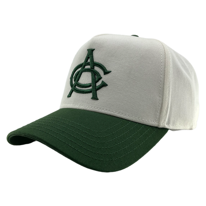 The OAC Logo 5 Panel by OAC is a white snapback cap with a dark green brim, featuring an embroidered green interlocked “A” and “C” logo on the front for the Oakland Athletic Club. Visible stitching accents the bill and crown, and it’s shown against a plain white background.