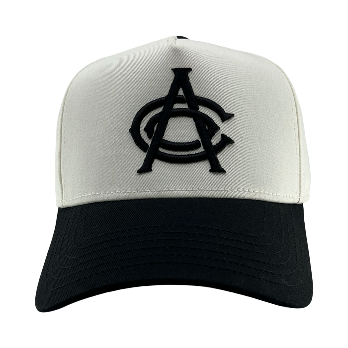 The OAC Logo 5 Panel by OAC is a two-tone snapback cap featuring a white crown, black bill, and bold black embroidered overlapping “CA” letters on the front center. Inspired by classic Oakland Athletic Club style, the cap faces directly forward against a plain white background.