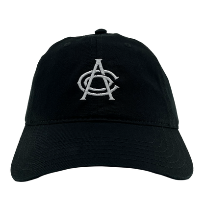 The OAC Logo Dad Hat by OAC is a black dad hat with white embroidered overlapping letters “A” and “C” on the front, symbolizing the Oakland Athletic Club. It features visible stitching along the slightly curved brim and includes an adjustable strap at the back. The product is shown against a plain white background.