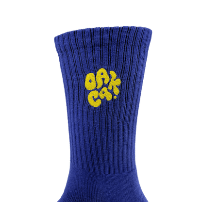 Close-up of embroidered yellow OAK CA blob-style wordmark on the side of blue crew sock.