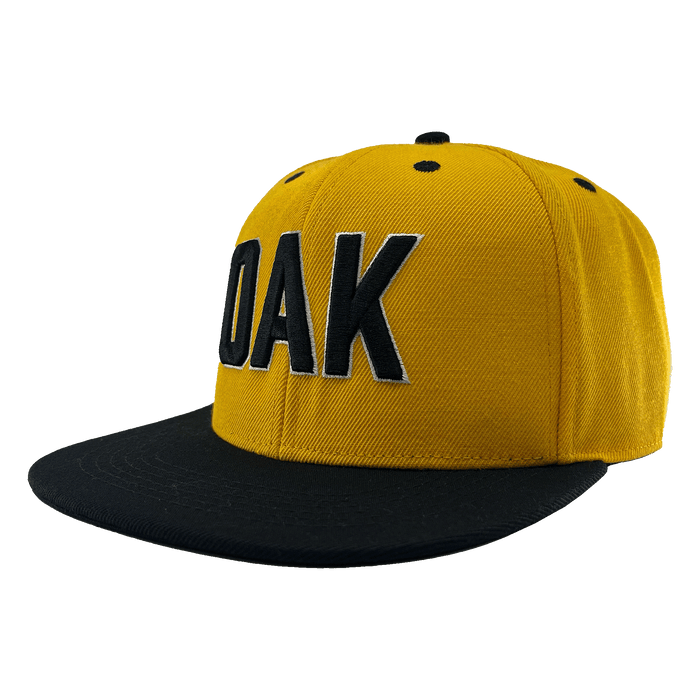 Angled side view of a yellow hat with a black flat bill, black embroidered details, and embroidered OAK block text on the front crown.