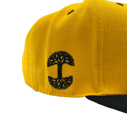 Side view of a yellow hat and black embroidered Oaklandish tree logo on the wearer's right side.
