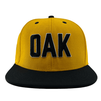 Front view of a yellow hat with a black flat bill, black embroidered details, and embroidered OAK block text on the front crown.