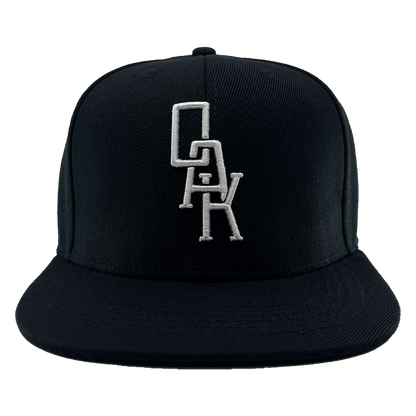 Front view of a black hat with a black bill and white embroidered OAK logo on the front crown.