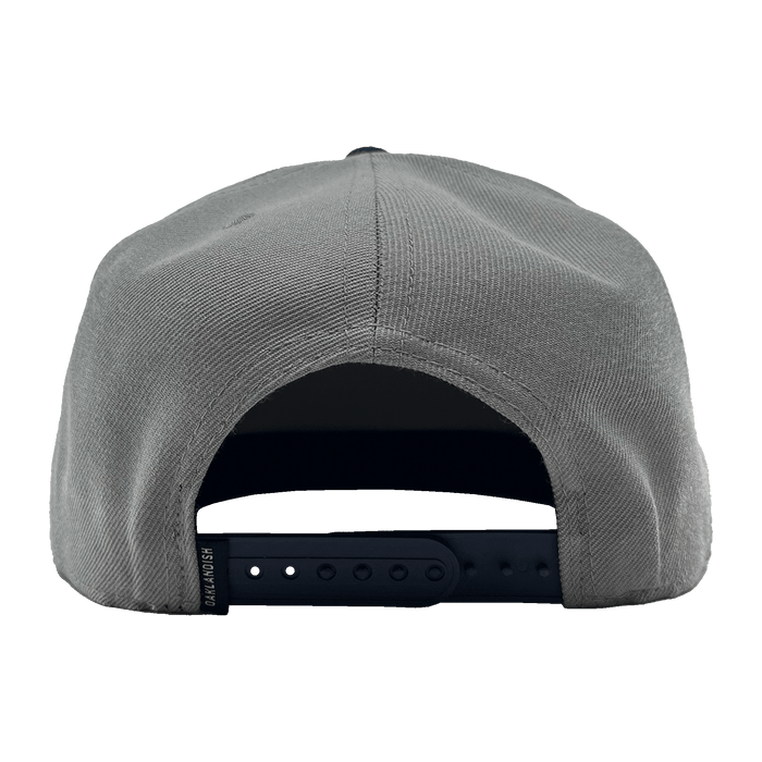 Rear view of the OAK Monogram Snapback in gray with an adjustable black snap closure. The fabric has a textured appearance, and the snap closure offers several adjustment holes. The inside of the back panel shows a partially visible sweatband. Simplistic in design, this cap features an embroidered OAK logo from Oaklandish.