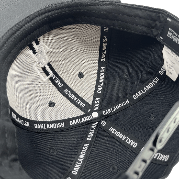 Inside crown view of a black cap with black striping with Oaklandish wordmark on repeat.