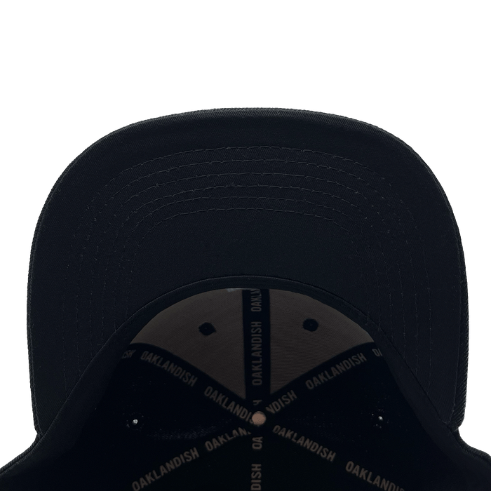 View of the underside of the bill of a black cap with black striping with Oaklandish wordmark on repeat inside the crown.