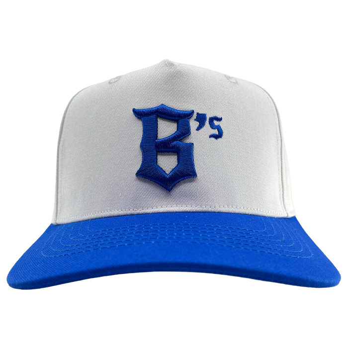 The Oakland Ballers 5 Panel Cap by Oakland Ballers is a white snapback featuring a vibrant blue brim. Centered on the front, it showcases a large, stylized blue “G” followed by a small blue apostrophe and the number “5” embroidered in classic Oakland Ballers style. The background is plain white.