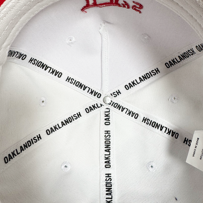 Inside view of the Oakland Ballers 5 Panel Cap shows white fabric panels with "OAKLANDISH" on black-edged seams, evoking local baseball pride. A white care tag and silver center button accent this Oakland Ballers hat.