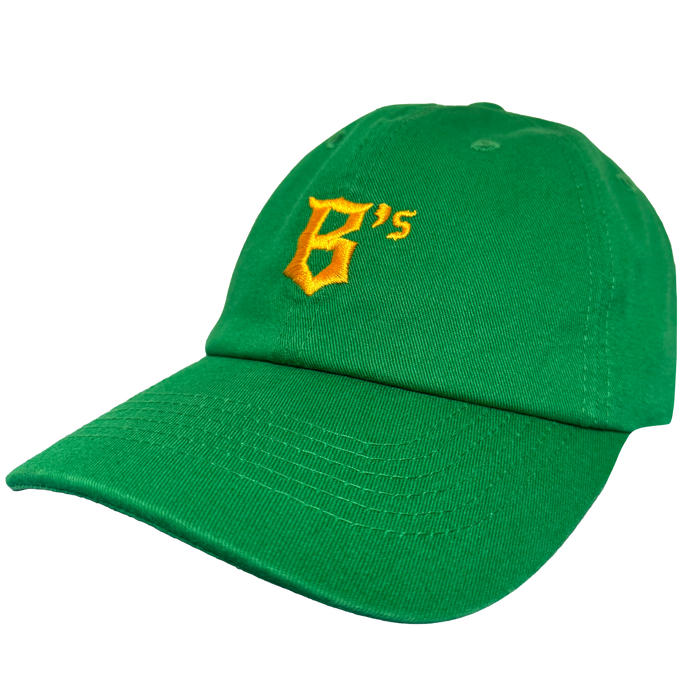 The Oakland Ballers Dad Hat by Oakland Ballers is a green cap with a yellow embroidered “B’s” on the front, inspired by the pro baseball team. It features a curved brim, visible stitching, and is shown against a plain white background.