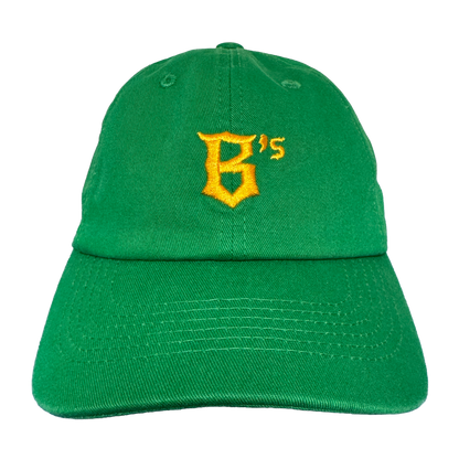 The Oakland Ballers Dad Hat features a green design with a yellow embroidered "B's" on the front, visible stitching, and a curved brim. The cap is photographed against a plain white background. Brand: Oakland Ballers.