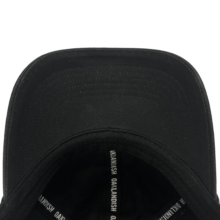 A close-up view of the Oakland Ballers Dad Hat, showcasing the underside of the brim and interior taping labeled "OAKLANDISH" in white text. The smooth black fabric and detailed stitching on the brim are clearly visible. Perfect for an Oakland Ballers fan, this hat embodies a community-focused experience.