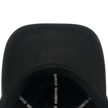 A close-up view of the Oakland Ballers Dad Hat, showcasing the underside of the brim and interior taping labeled "OAKLANDISH" in white text. The smooth black fabric and detailed stitching on the brim are clearly visible. Perfect for an Oakland Ballers fan, this hat embodies a community-focused experience.