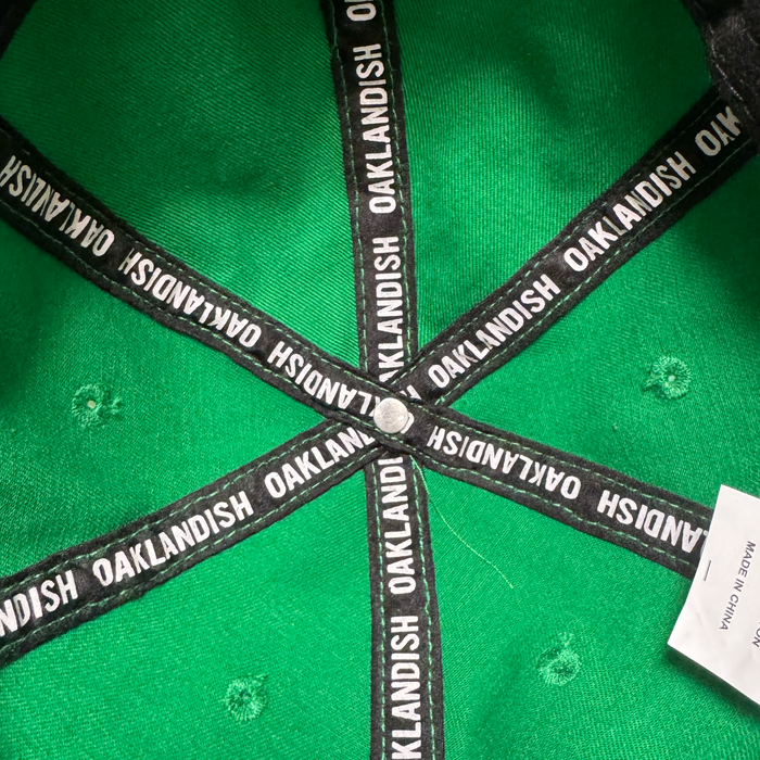 Inside the Oakland Ballers Dad Hat by Oakland Ballers: green with black trim, “OAKLANDISH” in white along the seams, a central metal button, and a partially visible white tag on the right. Inspired by Oakland's baseball spirit.