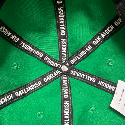 Inside the Oakland Ballers Dad Hat by Oakland Ballers: green with black trim, “OAKLANDISH” in white along the seams, a central metal button, and a partially visible white tag on the right. Inspired by Oakland's baseball spirit.
