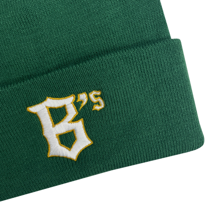 A close-up image of the Oakland Ballers Logo Beanie, a green knit hat with the letters "B's" embroidered on the fold to represent the Oakland Ballers professional baseball team. The text features a white, stylized font with a yellow outline. The beanie’s texture and stitching are clearly visible against the plain, light gray background.