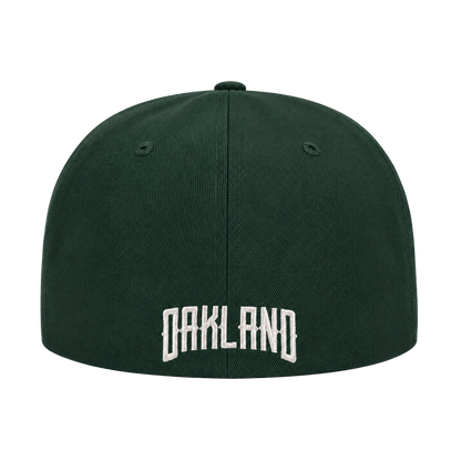 The Oakland Ballers Logo Hat by Oakland Ballers is a dark green baseball cap seen from the back, with "OAKLAND" embroidered in large white letters at the lower center and two ventilation holes per side. The background is plain white.
