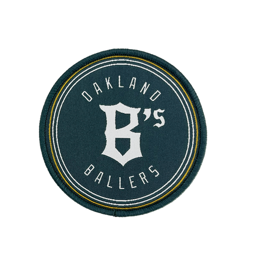 The Oakland Ballers Logo Patch from the Oakland Ballers features a circular design with a dark green background. The words "Oakland Ballers" are arched along the top and bottom edges, while a large, stylized white "B's" occupies the center. Representing the professional baseball team in the Pioneer League, this patch is bordered by thin white and yellow rings.