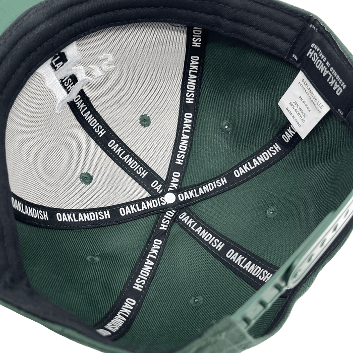 Interior view of the Oakland Ballers Snapback. The inside features black seams repeatedly labeled "OAKLANDISH" in white text. The label inside includes washing instructions and material information. The cap also has a small logo design on the inner top panel, celebrating the Oakland Ballers, a Pioneer League professional baseball team. The brim is lined with black fabric.