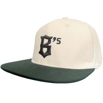 Introducing the Oakland Peloteros Hat by Oakland Ballers: This white cap features a dark green flat brim and showcases a prominent, black Gothic-style "B" with an adjoining apostrophe and "s" on the front—forming "B's," a proud symbol of the Oakland Ballers team from the Pioneer League. The background is crisp, clean white for a classic appeal.