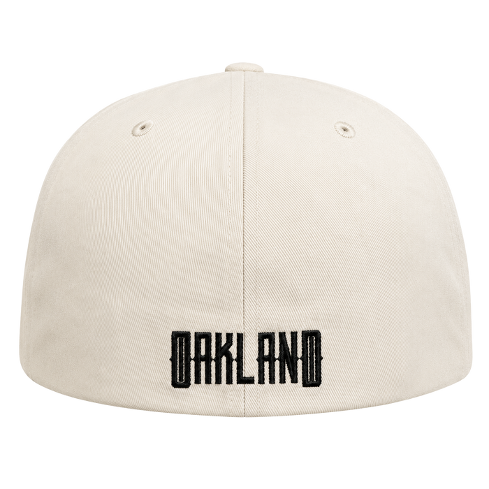A cream-colored Oakland Peloteros Hat from the Oakland Ballers is displayed from the back, featuring "OAKLAND" embroidered in bold, black block letters near the bottom—a tribute to the city's exciting new Pioneer League team. Two small eyelets appear on either side of the top center seam. The background is white.