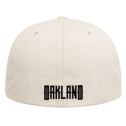 A cream-colored Oakland Peloteros Hat from the Oakland Ballers is displayed from the back, featuring "OAKLAND" embroidered in bold, black block letters near the bottom—a tribute to the city's exciting new Pioneer League team. Two small eyelets appear on either side of the top center seam. The background is white.