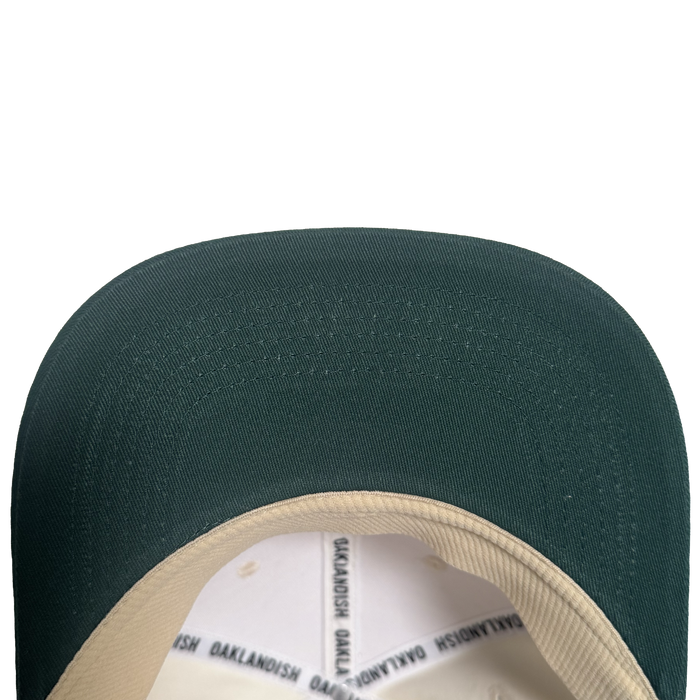 Close-up view of the brim and part of the inner lining of the Oakland Peloteros Hat by Oakland Ballers. The hat features a green brim and a beige inner lining with repeating black "OAKLANDISH" text. Set against a plain white background, only the top portion of this classic design is visible—a stylish nod to Oakland baseball team pride.