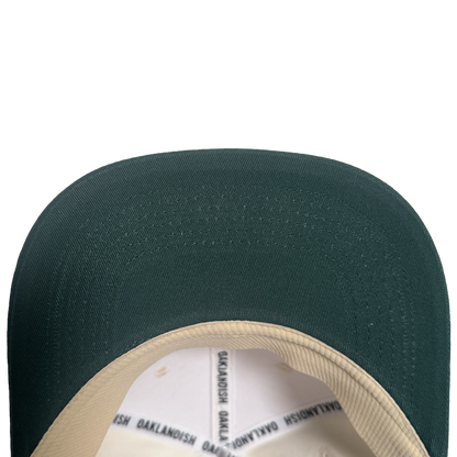 Close-up view of the brim and part of the inner lining of the Oakland Peloteros Hat by Oakland Ballers. The hat features a green brim and a beige inner lining with repeating black "OAKLANDISH" text. Set against a plain white background, only the top portion of this classic design is visible—a stylish nod to Oakland baseball team pride.