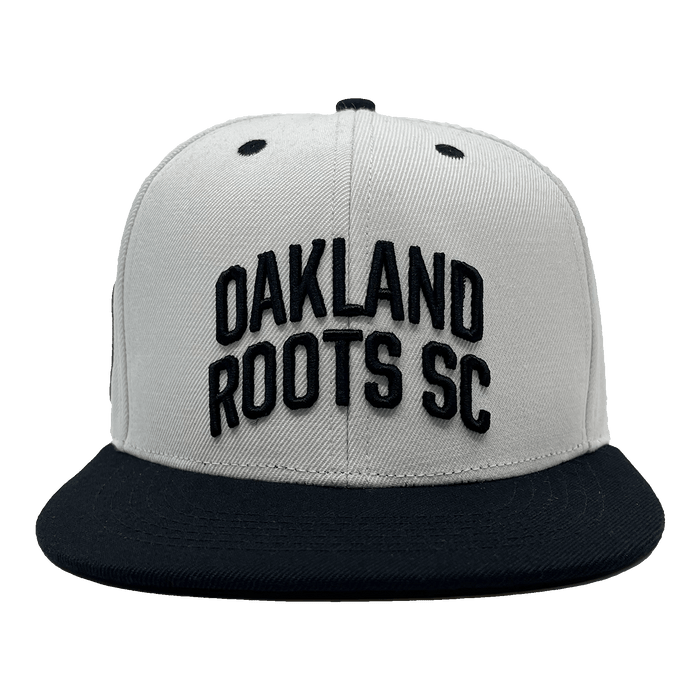 Introducing the Oakland Roots SC Arched Text Snapback by Oakland Roots SC: a gray snapback hat with a black brim. The front prominently displays "OAKLAND ROOTS SC" in bold, black, raised letters. Two small black eyelets on the top provide ventilation. The overall design is simple and sporty, capturing the essence of Oaklandish spirit that represents the Oakland Roots.