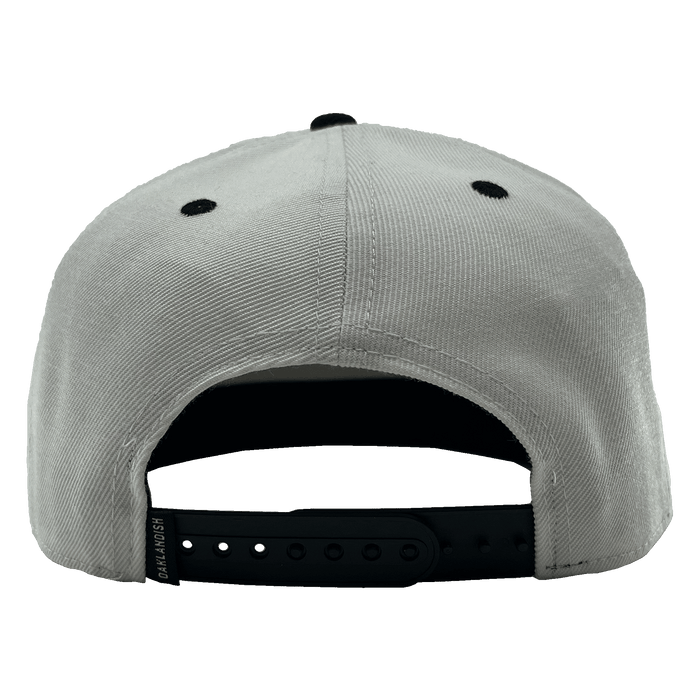 The Oakland Roots SC Arched Text Snapback is displayed from the back, highlighting black ventilation eyelets and a black adjustable snapback closure. The closure includes a branded tag with "DriLaunch" inscribed on it. Made from soft, slightly textured fabric, this light gray cap is ideal for any Oakland Roots supporter.