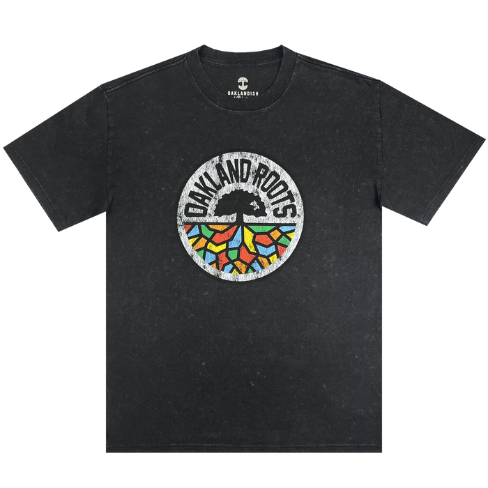 The Oakland Roots SC Classic Heavy Stone Wash Tee is a black, short-sleeved T-shirt that features a central circular logo. The logo showcases an abstract tree design with vibrant, geometric leaves and the text "Oakland Roots" arched above it, symbolizing the sports club's dedication to social good. The Oaklandish brand logo is printed near the collar for an added touch of authenticity.