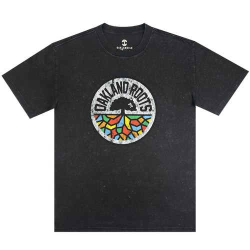 The Oakland Roots SC Classic Heavy Stone Wash Tee is a black, short-sleeved T-shirt that features a central circular logo. The logo showcases an abstract tree design with vibrant, geometric leaves and the text "Oakland Roots" arched above it, symbolizing the sports club's dedication to social good. The Oaklandish brand logo is printed near the collar for an added touch of authenticity.