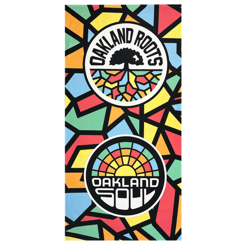 The Oakland Roots SC & Soul Towel by Oakland Roots SC is a brightly colored, premium dye-sublimated beach towel featuring a geometric mosaic pattern. It showcases two circular logos: one with a black tree and the text "OAKLAND ROOTS," and the other with a sunrise and the text "OAKLAND SOUL." The background displays vibrant shapes in red, yellow, green, blue, and black. Proceeds from this product support social good initiatives by the Oakland Roots Sports Club.