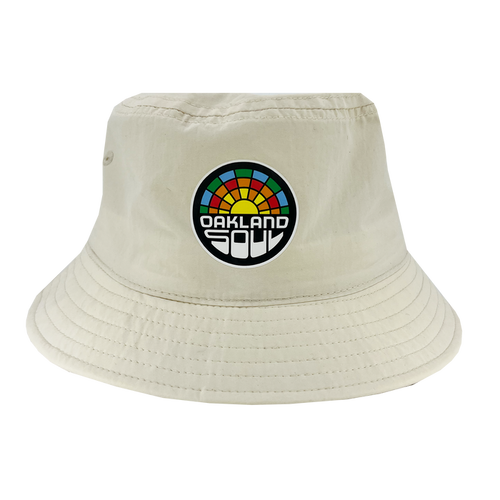 The Oakland Soul Logo Bucket Hat, a beige hat adorned with the "Oakland Soul" logo on the front, celebrates our local women's soccer team in the USL W-League. The logo features a vibrant, semi-circular sunset design with "Oakland Soul" prominently displayed in bold black and white letters below it. Visible stitching around the brim adds to its detail.