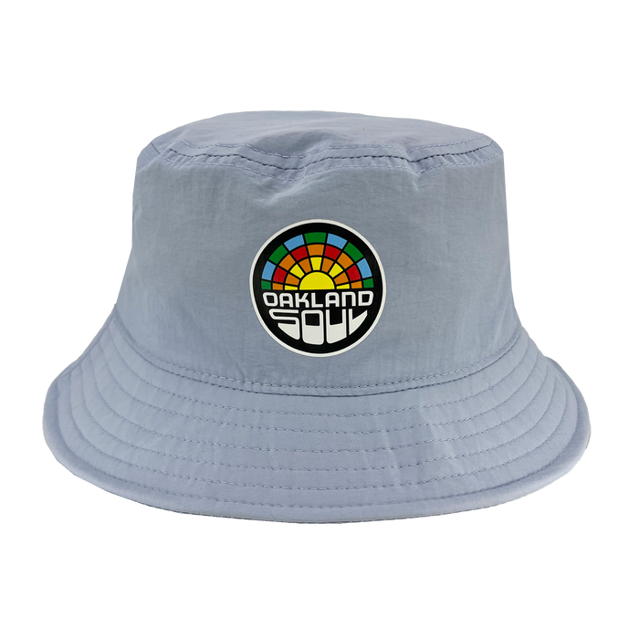 The Oakland Soul Logo Bucket Hat by Oakland Soul is a light blue accessory adorned with a colorful rainbow patch and the words "Oakland Soul" in bold white and black font on the front. Inspired by Oakland's women's soccer team, this hat features a soft, unstructured brim with visible stitching around the edges.