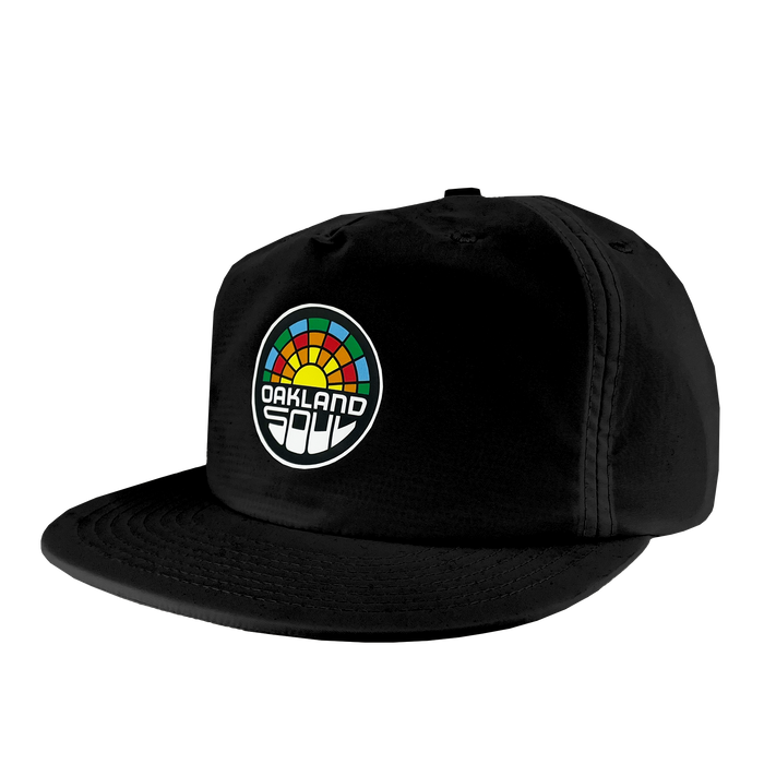 The Oakland Soul Surf Cap is a black snapback hat boasting a vibrant geometric design reminiscent of a sunrise or sunset on the front panel. Below this design, the text "OAKLAND SOUL" is prominently displayed in honor of the women's soccer team from the USL W-League. The hat features a slightly curved bill and noticeable stitching details.
