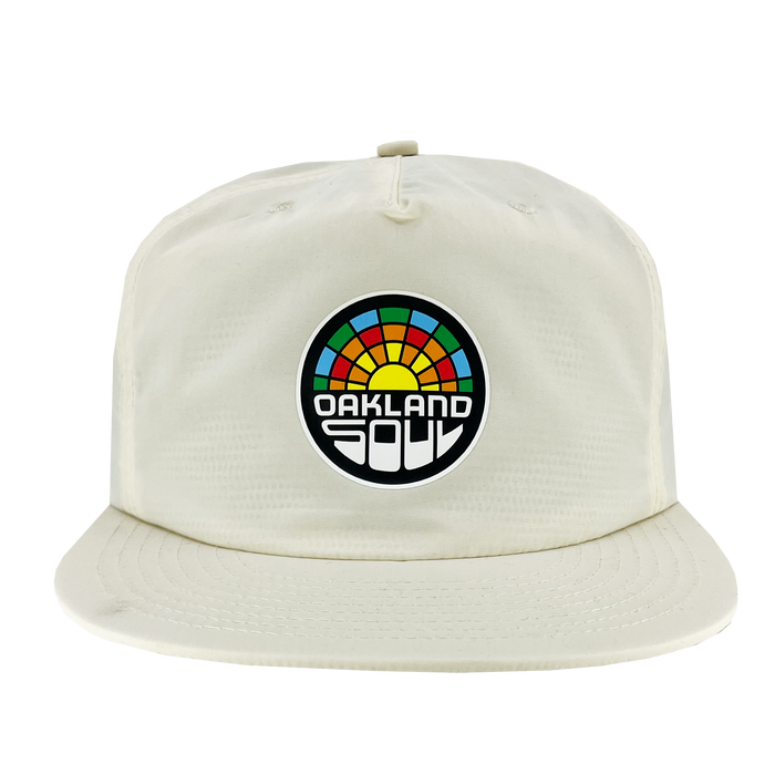 The Oakland Soul Surf Cap, a white baseball cap with a flat brim, showcases a circular logo on the front. The logo features a colorful, semi-circular design resembling a sunrise or rainbow with "OAKLAND SOUL" in bold white letters against a black background, celebrating Oakland Soul, our women's soccer team in the USL W-League.