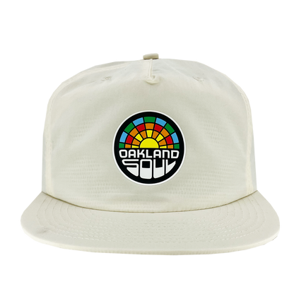 The Oakland Soul Surf Cap, a white baseball cap with a flat brim, showcases a circular logo on the front. The logo features a colorful, semi-circular design resembling a sunrise or rainbow with "OAKLAND SOUL" in bold white letters against a black background, celebrating Oakland Soul, our women's soccer team in the USL W-League.