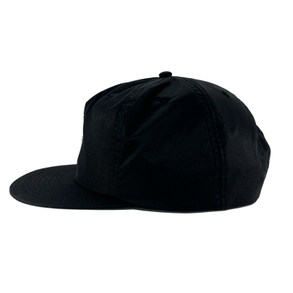 A side view of the Oakland Soul Surf Cap is depicted against a white background. This black cap features a flat brim and a structured crown, complemented by a button on top and stitch detailing along the seams and brim. Reflecting the dynamic spirit of Oakland Soul in the USL W-League, the cap appears plain with no visible logos or designs.
