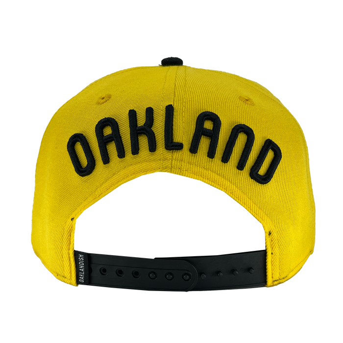 Back view of yellow snapback hat with 'Oakland' text above arch and oaklandish woven label near black plastic closure.