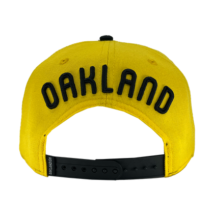 Back view of yellow snapback hat with 'Oakland' text above arch and oaklandish woven label near black plastic closure.