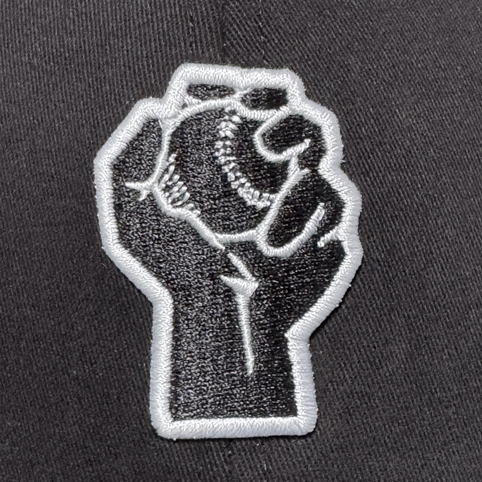 The Oakland Stand Up Hat by Oakland Ballers features a black and white embroidered patch of a raised fist holding a baseball, symbolizing solidarity and the spirit of the city’s newest Pioneer League team.