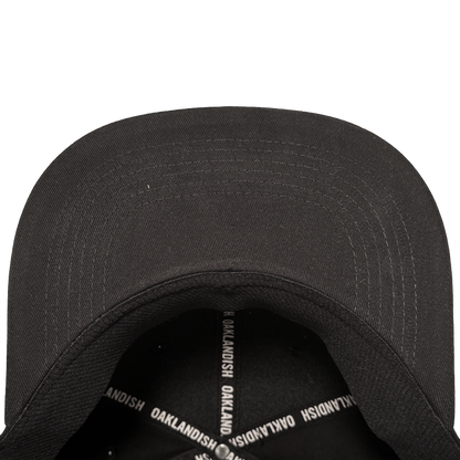 A close-up, top-down view of the Oakland Stand Up Hat by Oakland Ballers, showing its curved-brim black cap, visible stitching, and interior sweatband with crossed bands reading "OAKLANDISH," honoring Oakland’s baseball team spirit.