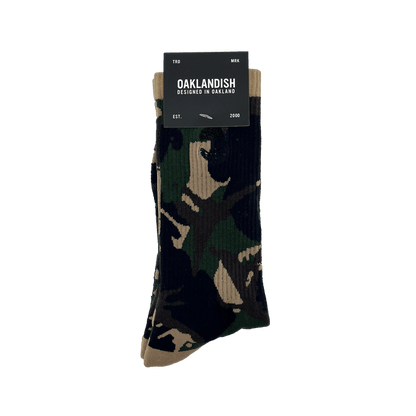 Pair folded camo crew socks in Oaklandish packaging with an embroidered black Oaklandish tree logo on the side.