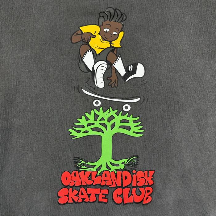 A cartoon of a smiling person with dark skin, gray hair, yellow shirt, white socks, and black shorts skating above a green tree. "OAKLANDISH SKATE CLUB" in bold red text appears below. Oaklandish Skate Club Hoodie by Oaklandish.